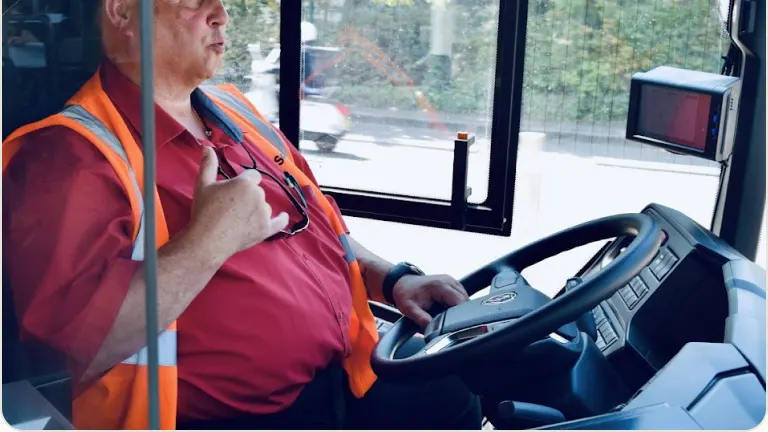 Un conducteur de bus en gilet orange, au volant, explique son quotidien de travail.