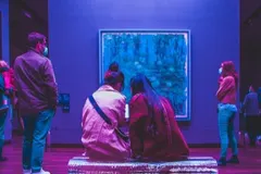 Des visiteurs d’un musée devant un tableau, dans une salle éclairée en bleu.
